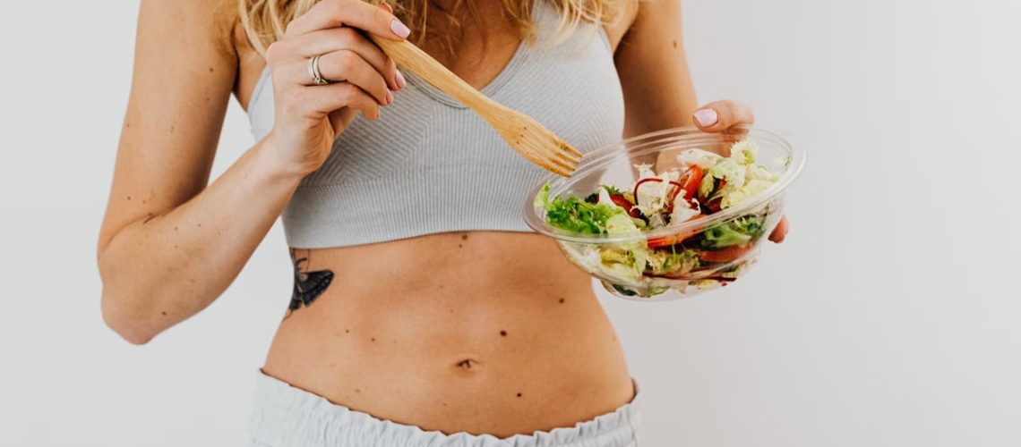 Young woman in sports attire holding a fresh salad bowl, promoting a healthy lifestyle.